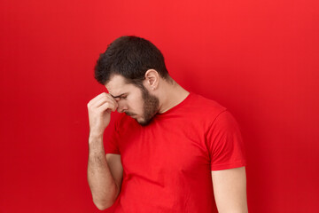 Young hispanic man wearing casual red t shirt tired rubbing nose and eyes feeling fatigue and headache. stress and frustration concept.