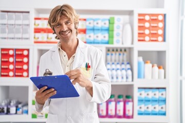 Young man pharmacist writing on clipboard at pharmacy