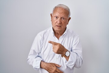 Senior man with grey hair standing over isolated background pointing aside worried and nervous with...