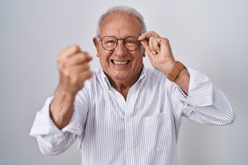 Obraz premium Senior man with grey hair holding glasses with hand annoyed and frustrated shouting with anger, yelling crazy with anger and hand raised