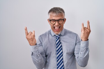 Hispanic business man with grey hair wearing glasses shouting with crazy expression doing rock symbol with hands up. music star. heavy music concept.