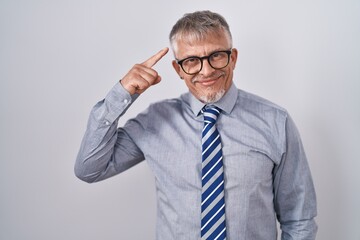 Hispanic business man with grey hair wearing glasses smiling pointing to head with one finger, great idea or thought, good memory