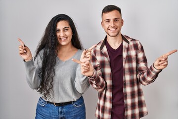 Young hispanic couple standing over white background smiling confident pointing with fingers to different directions. copy space for advertisement