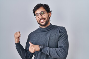 Handsome latin man standing over isolated background pointing to the back behind with hand and thumbs up, smiling confident