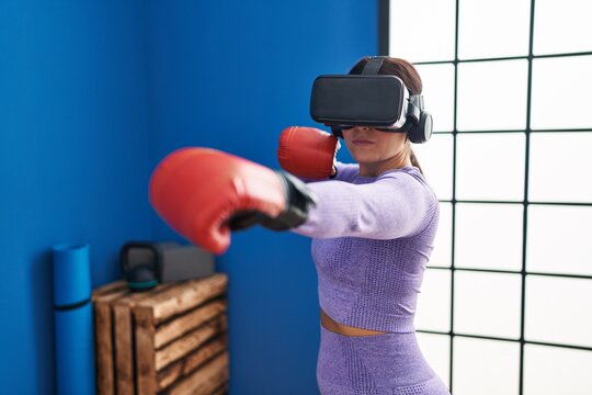 Young beautiful hispanic woman using virtual reality glasses boxing at sport center