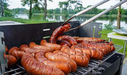 Man turning the sausage on the bbq with kitchen tongs. Person grilling in the garden. Barbeque with...