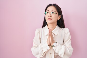 Young chinese woman standing over pink background begging and praying with hands together with hope...
