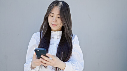 Young chinese woman using smartphone with serious expression over isolated white background