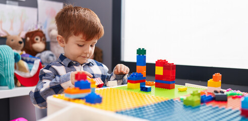 Adorable toddler playing with construction blocks sitting on table at kindergarten