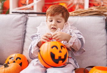 Adorable toddler wearing harlequin costume holding pumpkin basket at home