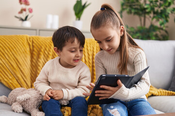 Adorable boy and girl using touchpad sitting on sofa at home
