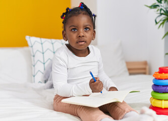 African american girl sitting on bed drawing on notebook at bedroom