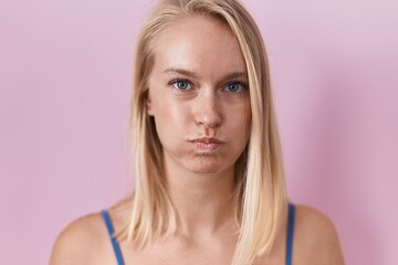Young caucasian woman standing over pink background puffing cheeks with funny face. mouth inflated...