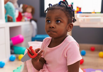 African american girl sitting on floor holding tool at kindergarten