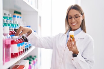 Young beautiful hispanic woman pharmacist smiling confident holding pills bottle at pharmacy