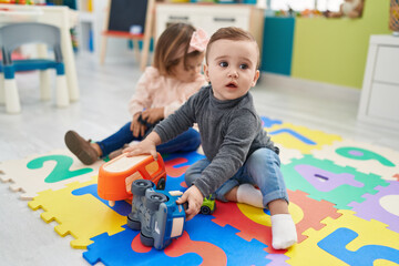 Adorable boy and girl playing with cars toy sitting on floor at kindergarten