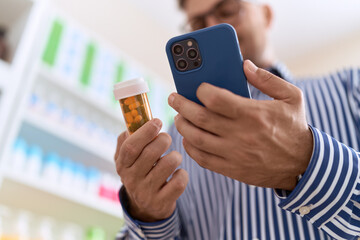 Young hispanic man customer using smartphone holding pills bottle at pharmacy