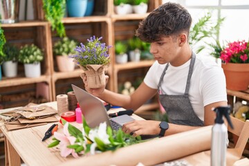 Young hispanic teenager florist using laptop holding lavender plant at flower shop