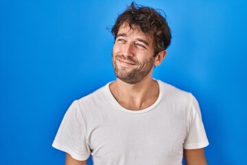 Fototapeta premium Hispanic young man standing over blue background smiling looking to the side and staring away thinking.