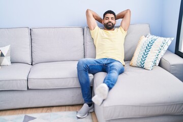 Young arab man relaxed with hands on head sitting on sofa at home