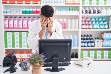 Hispanic man with beard working at pharmacy drugstore with sad expression covering face with hands...