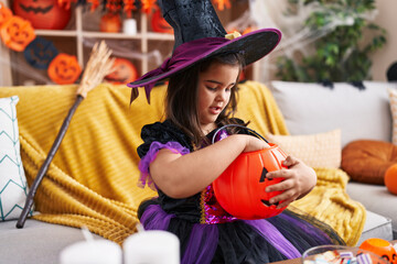 Adorable hispanic girl having halloween party holding sweet of pumpkin basket at home