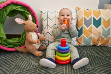 Obraz premium Adorable caucasian baby sitting on floor sucking hoops at home