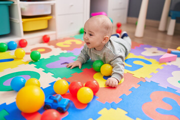 Adorable caucasian baby playing with balls lying on floor at kindergarten