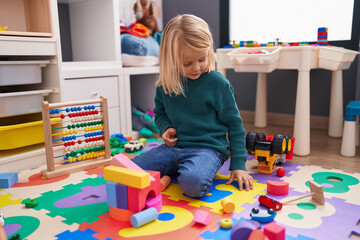 Adorable caucasian boy playing with car toy and construction blocks sitting on floor at kindergarten