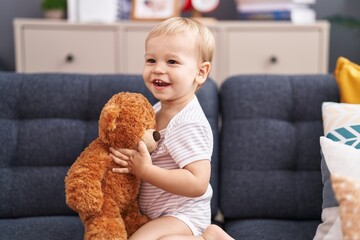 Adorable toddler playing with teddy bear sitting on sofa at home