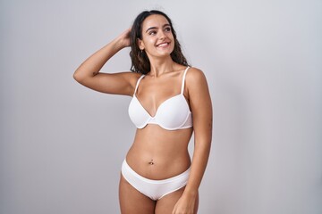 Fototapeta premium Young hispanic woman wearing white lingerie smiling confident touching hair with hand up gesture, posing attractive and fashionable