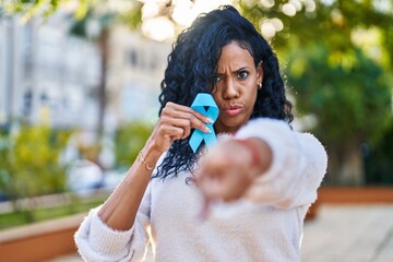 Obraz premium Middle age hispanic woman holding blue ribbon pointing with finger to the camera and to you, confident gesture looking serious