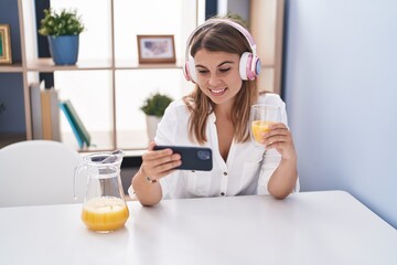 Young woman watching video on smartphone drinking orange juice at home