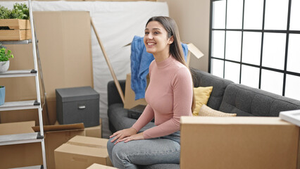 Young beautiful hispanic woman smiling proud sitting on sofa at new home