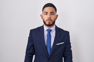 Young hispanic man wearing business suit and tie relaxed with serious expression on face. simple...