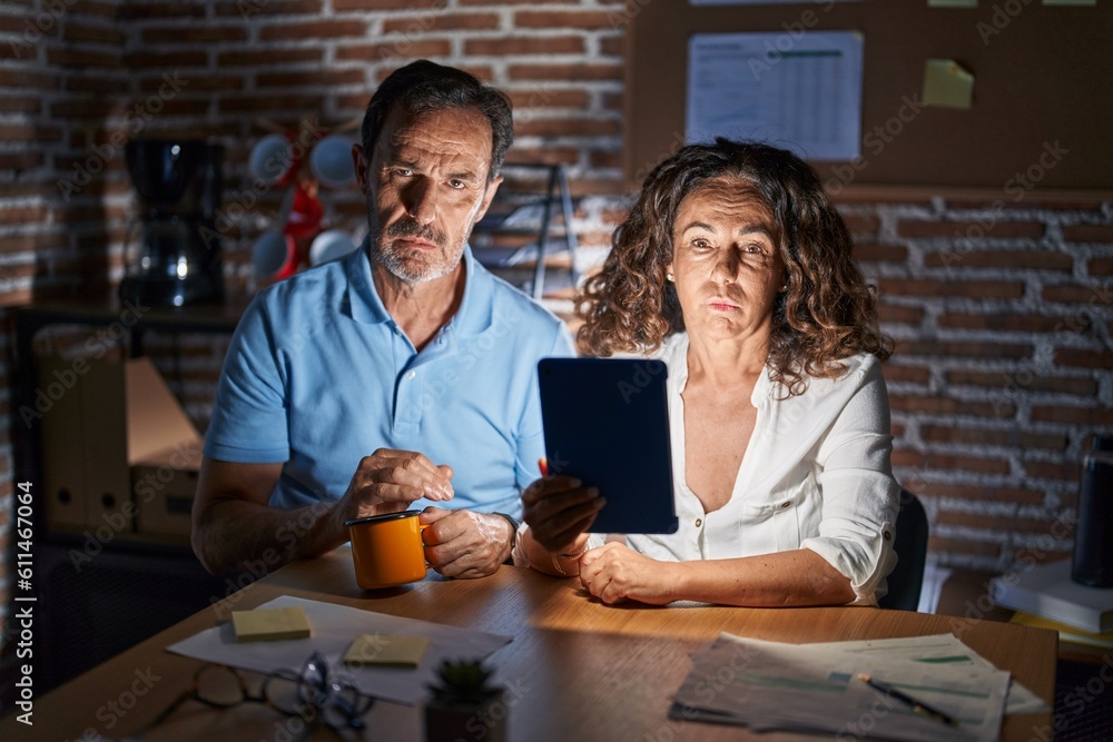 Poster middle age hispanic couple using touchpad sitting on the table at night looking sleepy and tired, ex