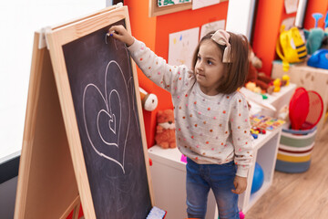Adorable hispanic girl drawing on blackboard at kindergarten