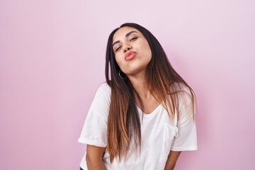Young arab woman standing over pink background looking at the camera blowing a kiss on air being lovely and sexy. love expression.