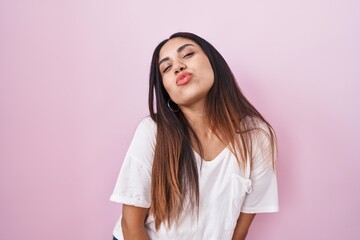 Obraz premium Young arab woman standing over pink background looking at the camera blowing a kiss on air being lovely and sexy. love expression.