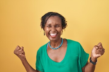 African woman with dreadlocks standing over yellow background very happy and excited doing winner gesture with arms raised, smiling and screaming for success. celebration concept.