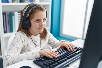 Adorable blonde girl student using computer and headphones studying at classroom