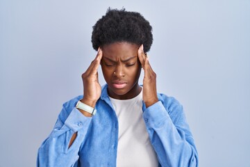 African american woman standing over blue background with hand on head, headache because stress. suffering migraine.