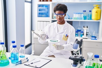 African american woman wearing scientist uniform using magnifying glass at laboratory