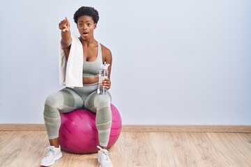 African american woman wearing sportswear sitting on pilates ball pointing with finger surprised...