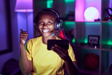 African american woman playing video games with smartphone smiling happy and positive, thumb up doing excellent and approval sign
