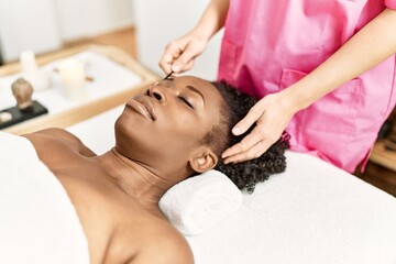 Fototapeta na wymiar African american woman lying on massage table having eyebrows treatment at beauty salon