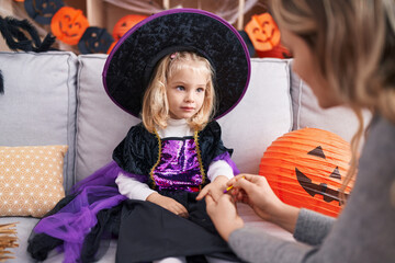 Adorable blonde girl sitting on sofa having halloween make up on hand at home