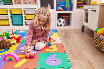 Adorable blonde girl playing with toys sitting on floor at kindergarten