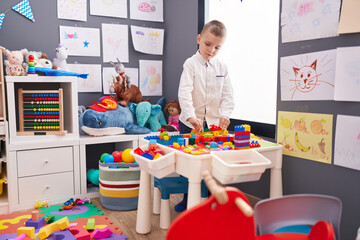 Adorable caucasian boy playing with construction blocks standing at kindergarten