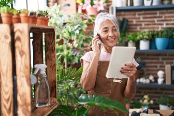 Middle age grey-haired woman florist talking on smartphone reading book at florist